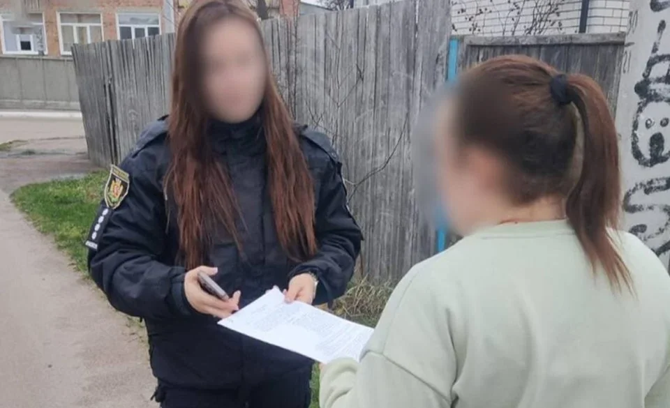 Поліцейська показує документ жінці біля дерев’яного паркану